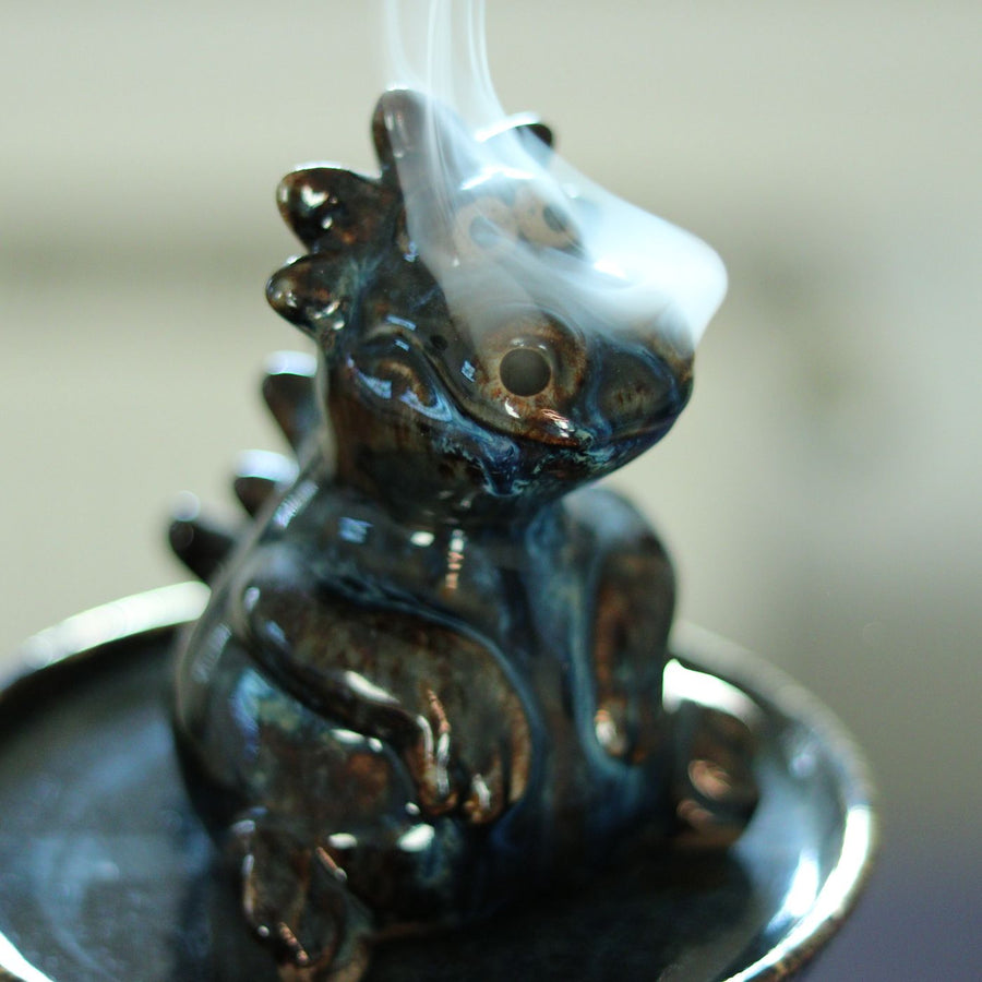A dragon incense burner indoors with thin wisps of smoke coming off it.