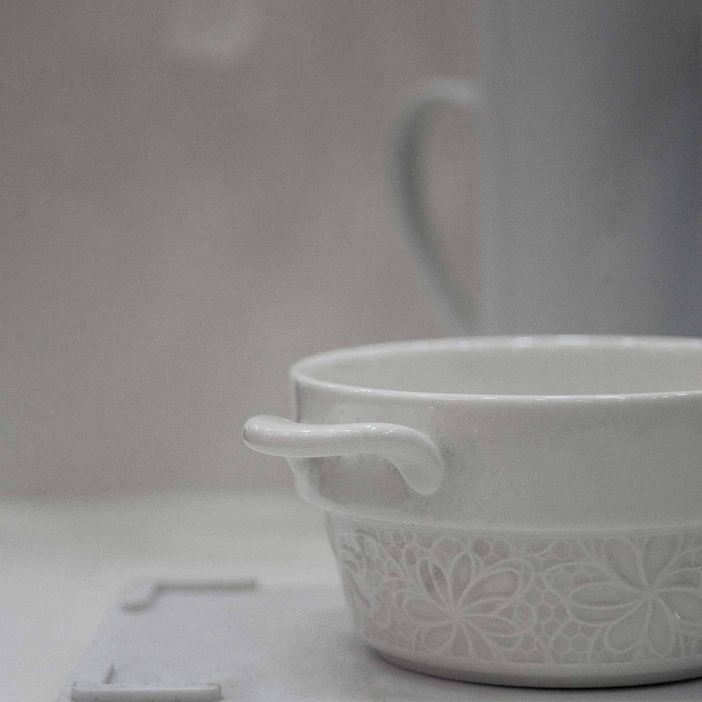 A white ceramic bowl with decorative surface work, shown close up on a grey background.