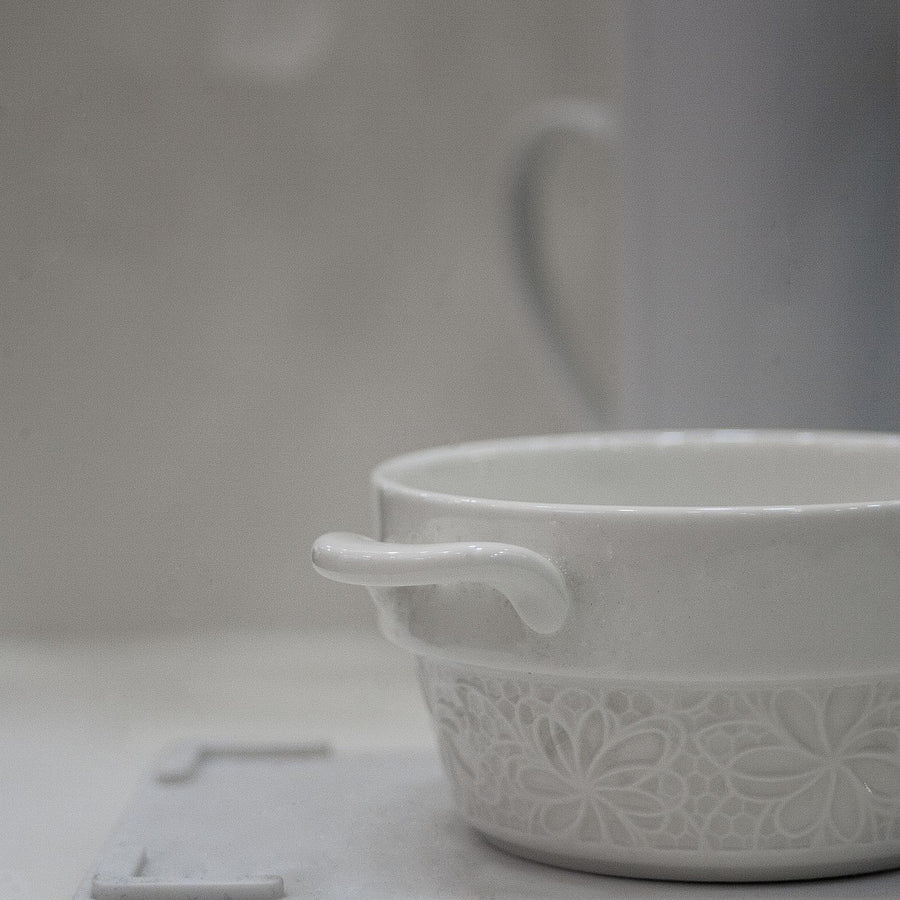 A white ceramic bowl with decorative surface work, shown close up on a grey background.