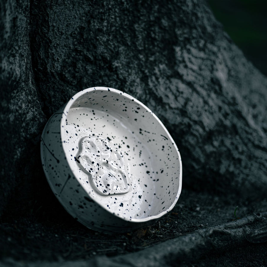 A speckled ceramic bowl resting against a tree trunk outdoors.