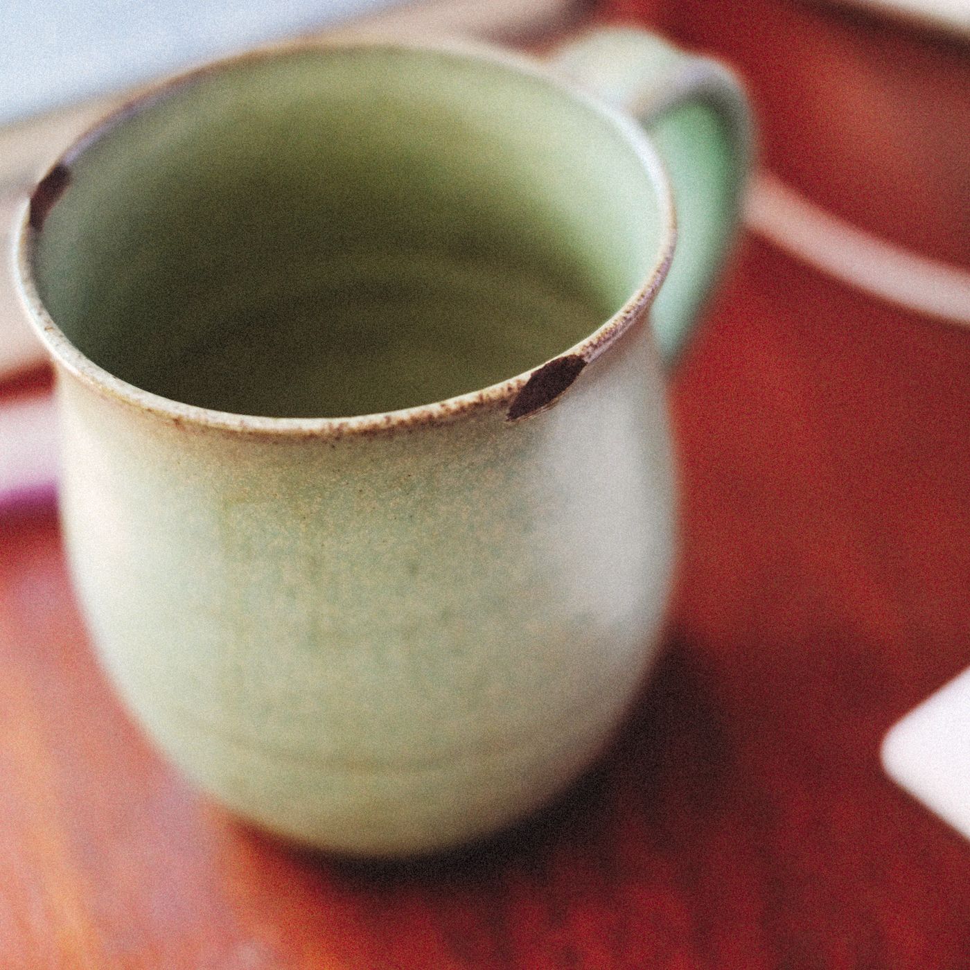A rustic green mug on a wooden table, photographed close enough to read the texture of the surface.