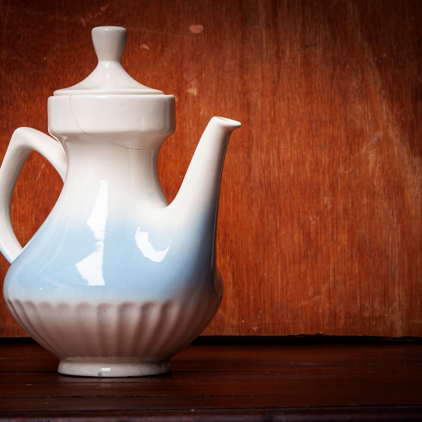 A white ceramic teapot photographed close up against a dark wooden background.