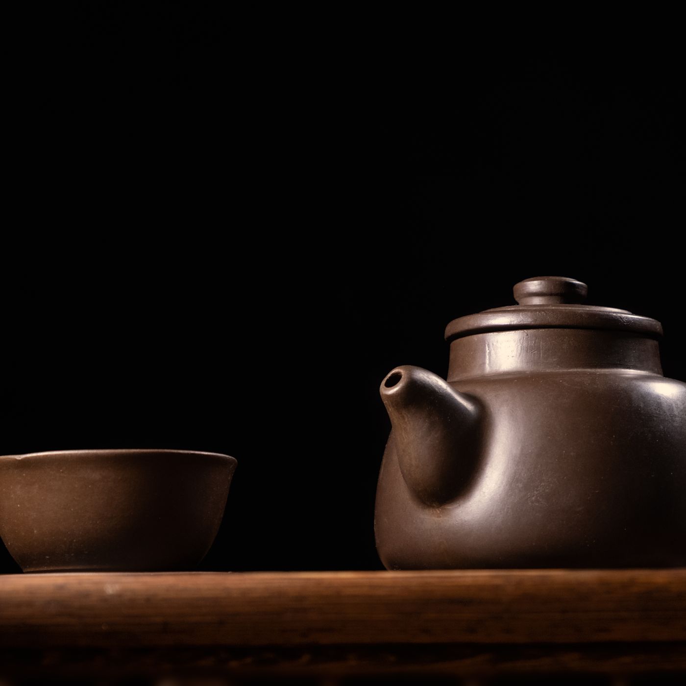 A Zisha teapot with a single cup, photographed as a still life against a dark background.
