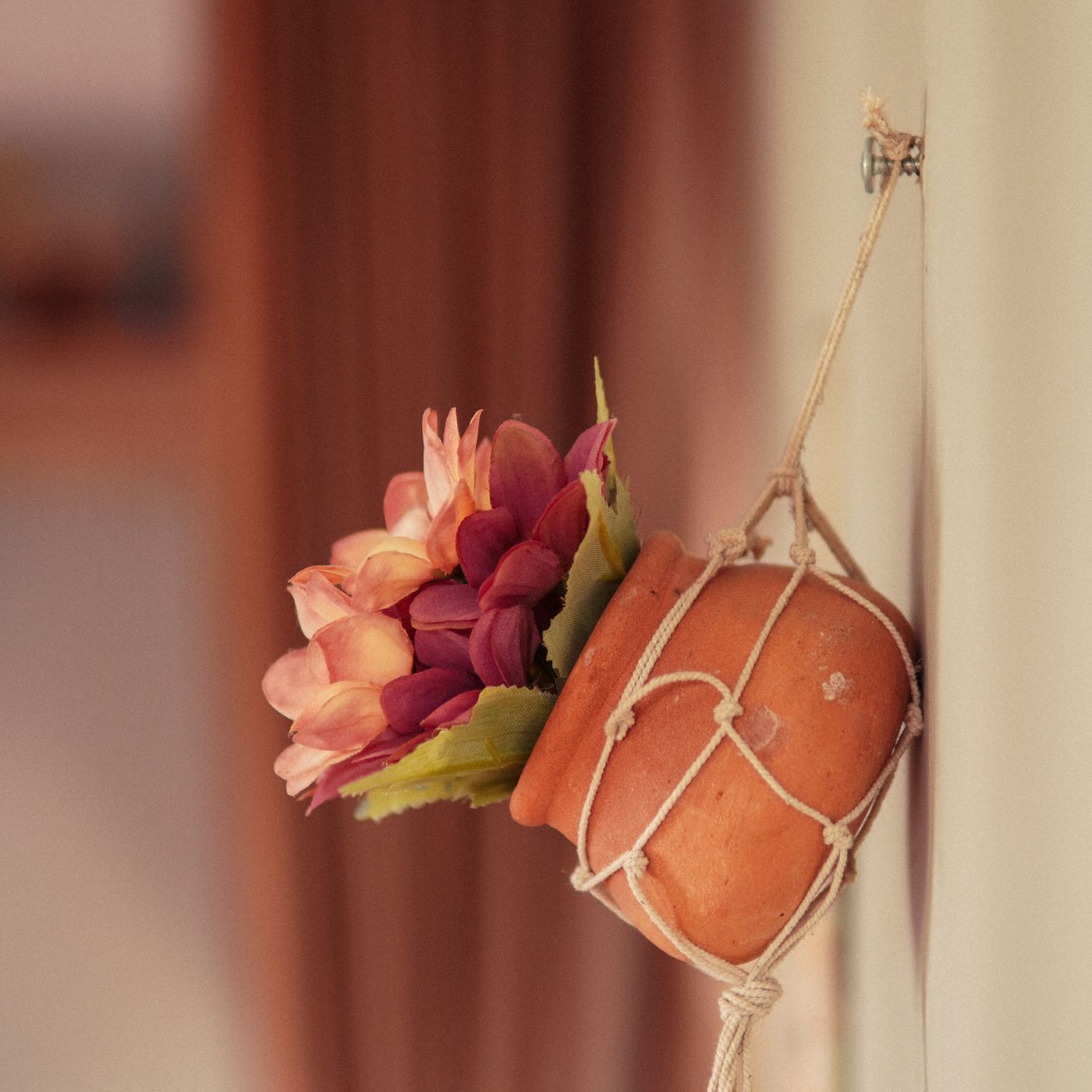 A terracotta pot held in a string hanger and mounted on a wall.
