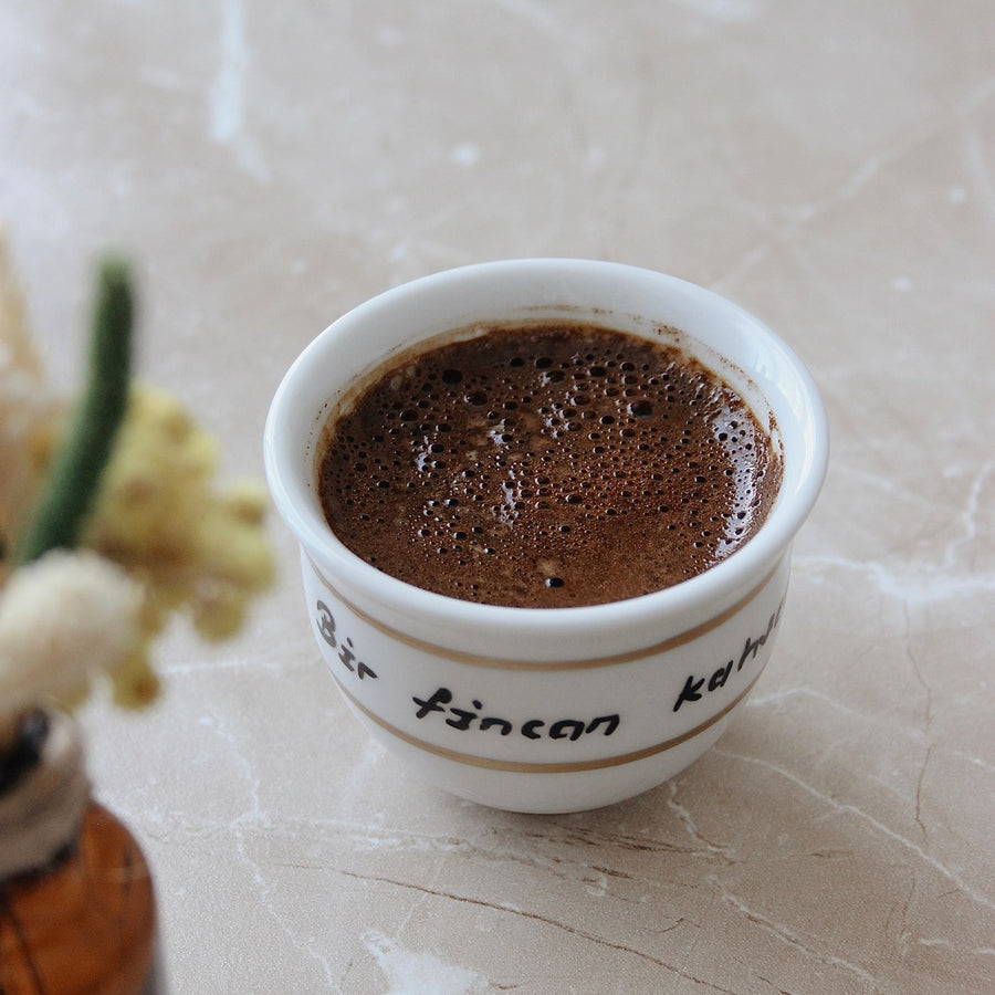 A Turkish coffee cup photographed close up on a marble table with floral decoration nearby.