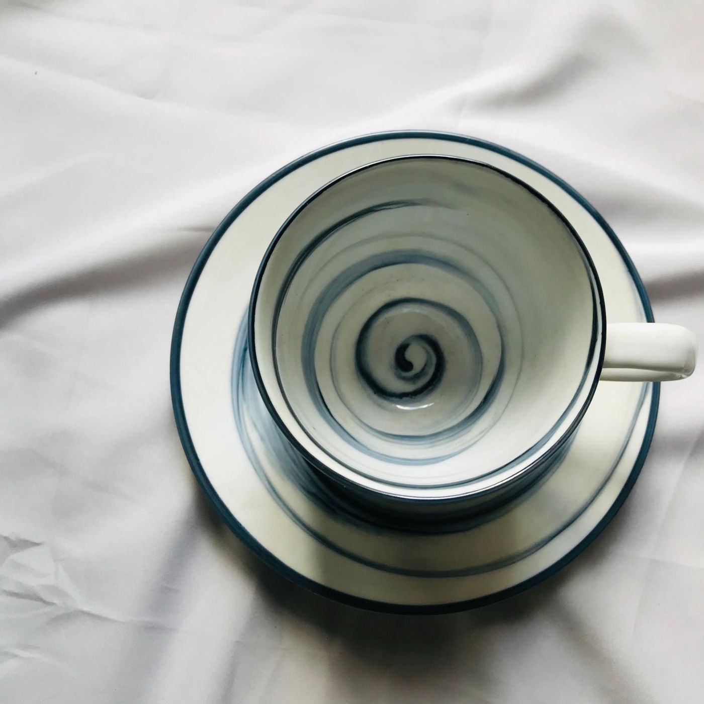 A ceramic teacup carrying a spiral pattern, photographed sitting on its matching saucer.