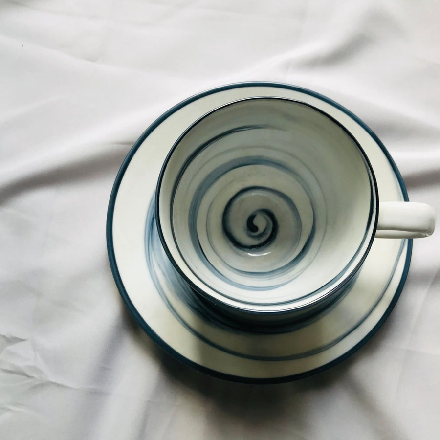 A ceramic teacup carrying a spiral pattern, photographed sitting on its matching saucer.