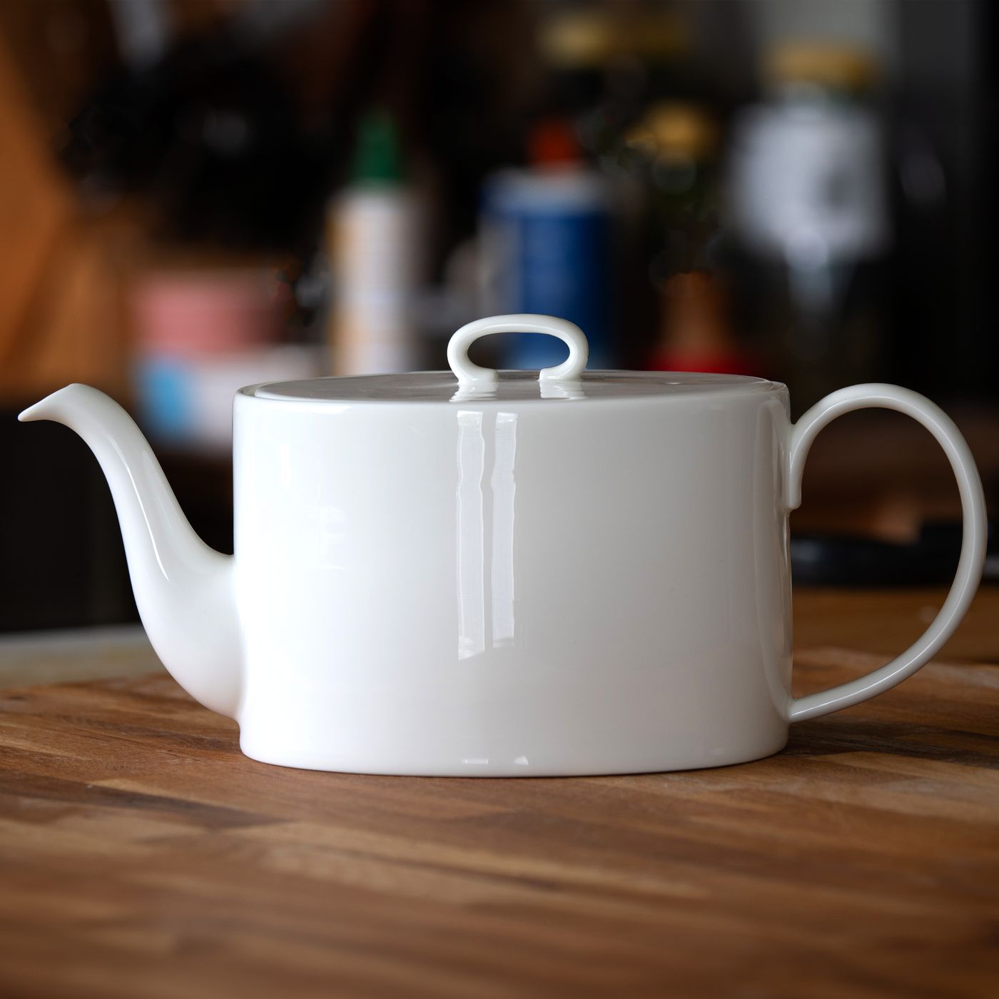 A white porcelain teapot on a wooden table in a kitchen.