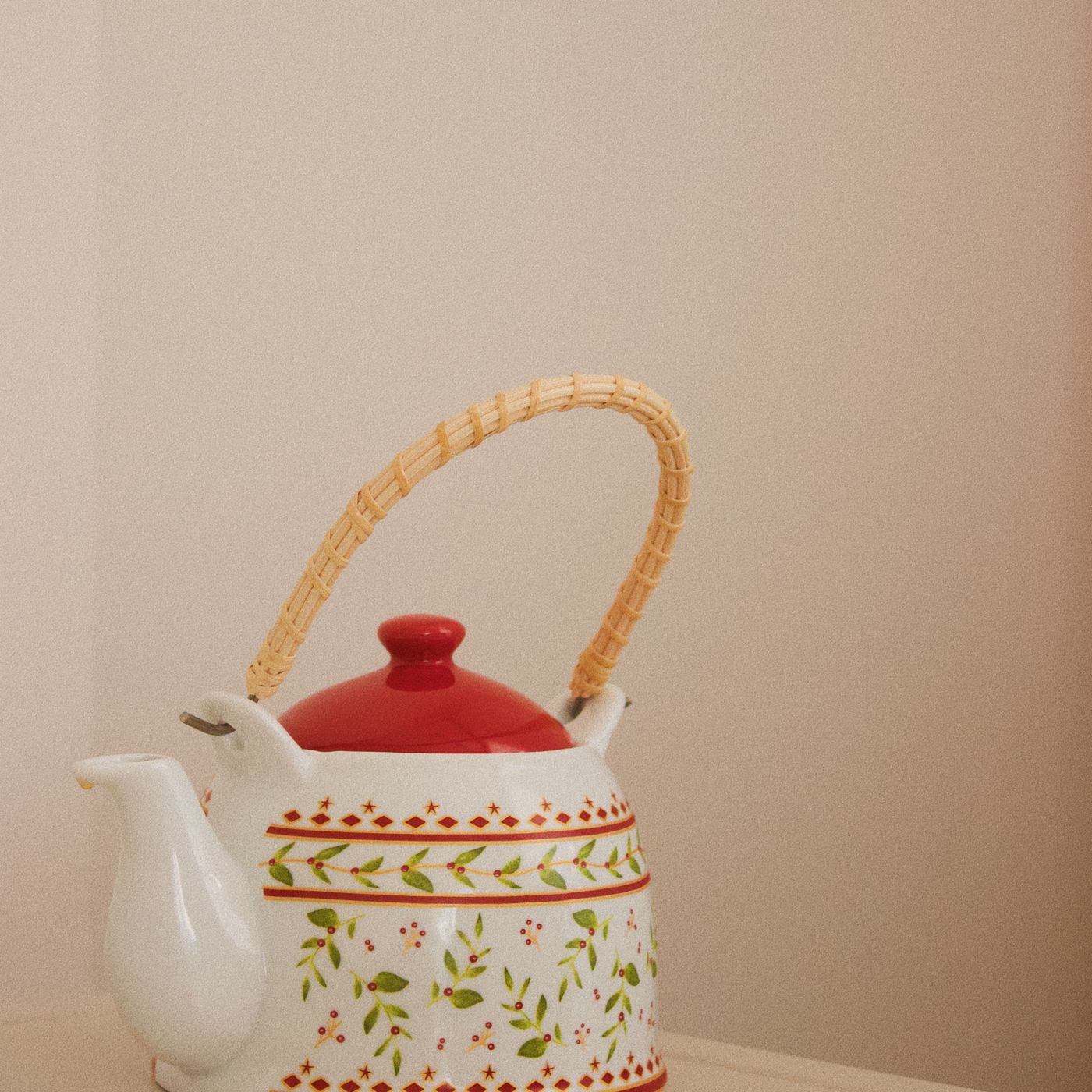 A floral teapot fitted with a wicker handle over the top.