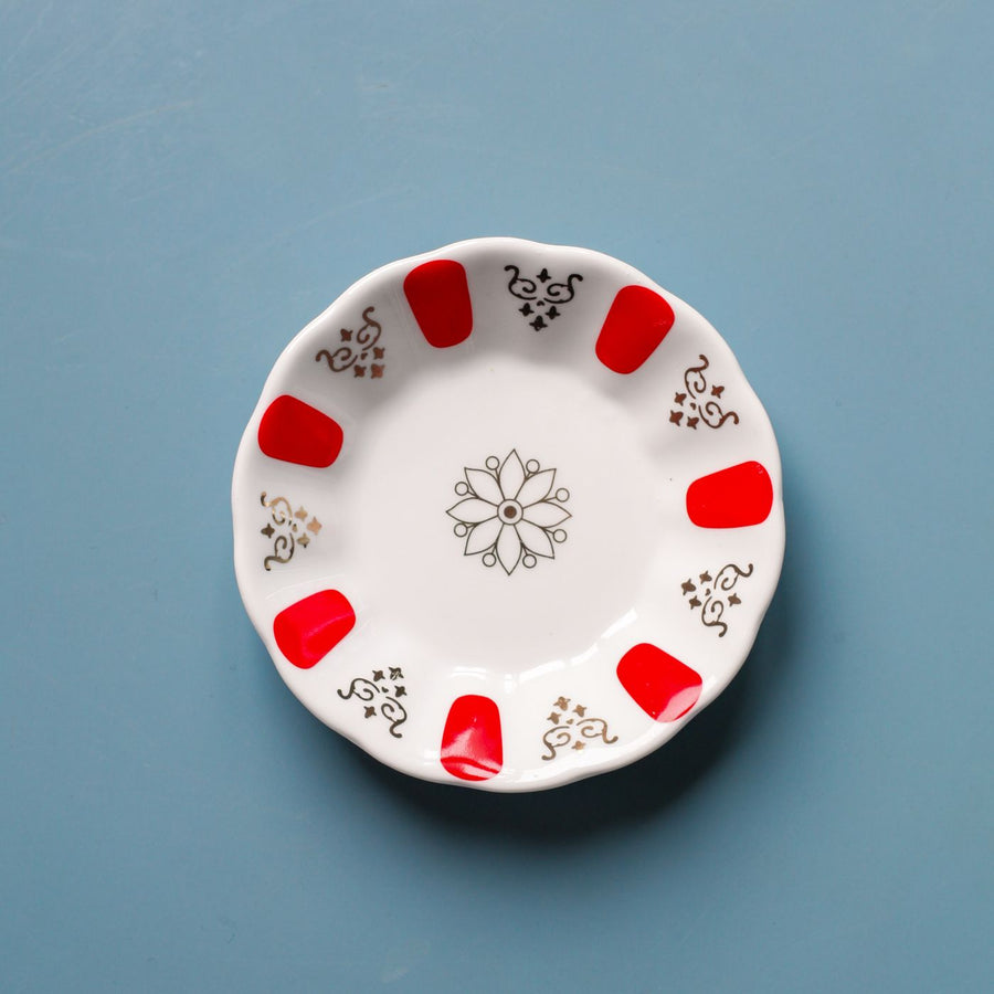 A decorative ceramic plate with red accents, shot from directly above on a blue background.