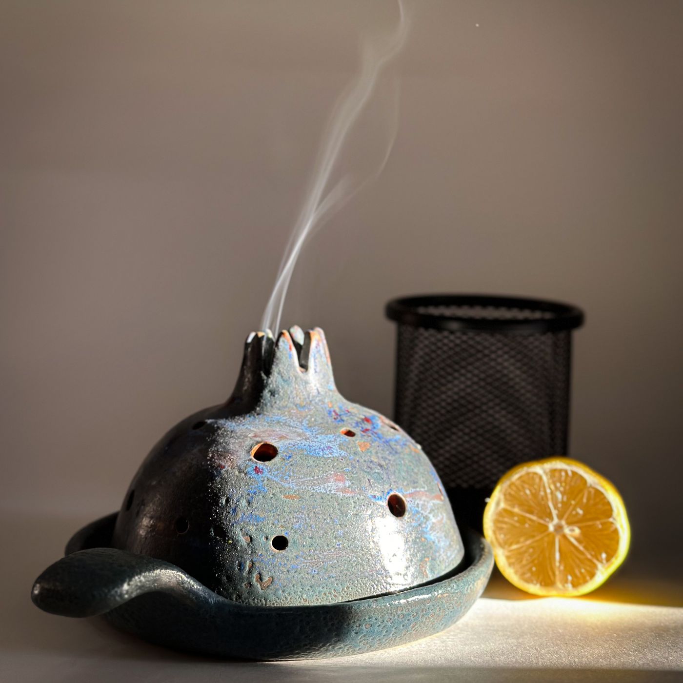 A ceramic incense burner giving off smoke, photographed beside a slice of lemon.