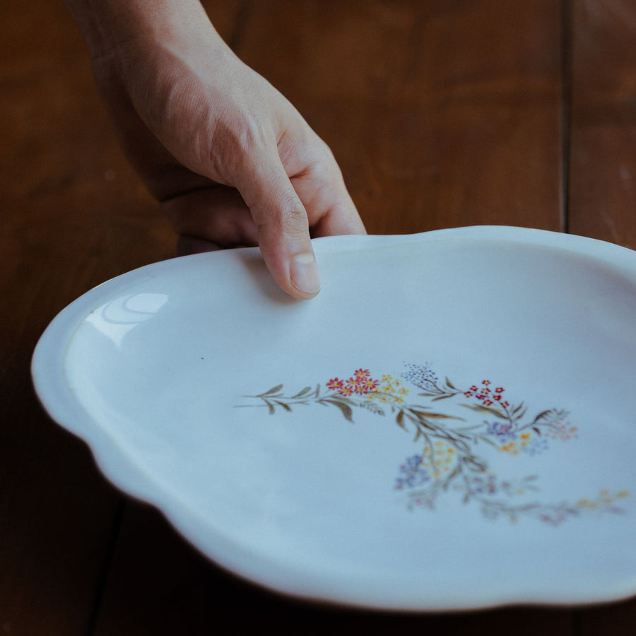 A floral ceramic plate being set down on a wooden table, vintage in character.