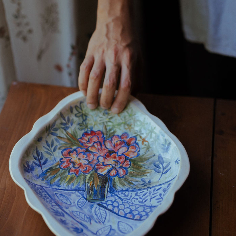 A decorative floral plate held in one hand above a wooden table, which gives its size away.