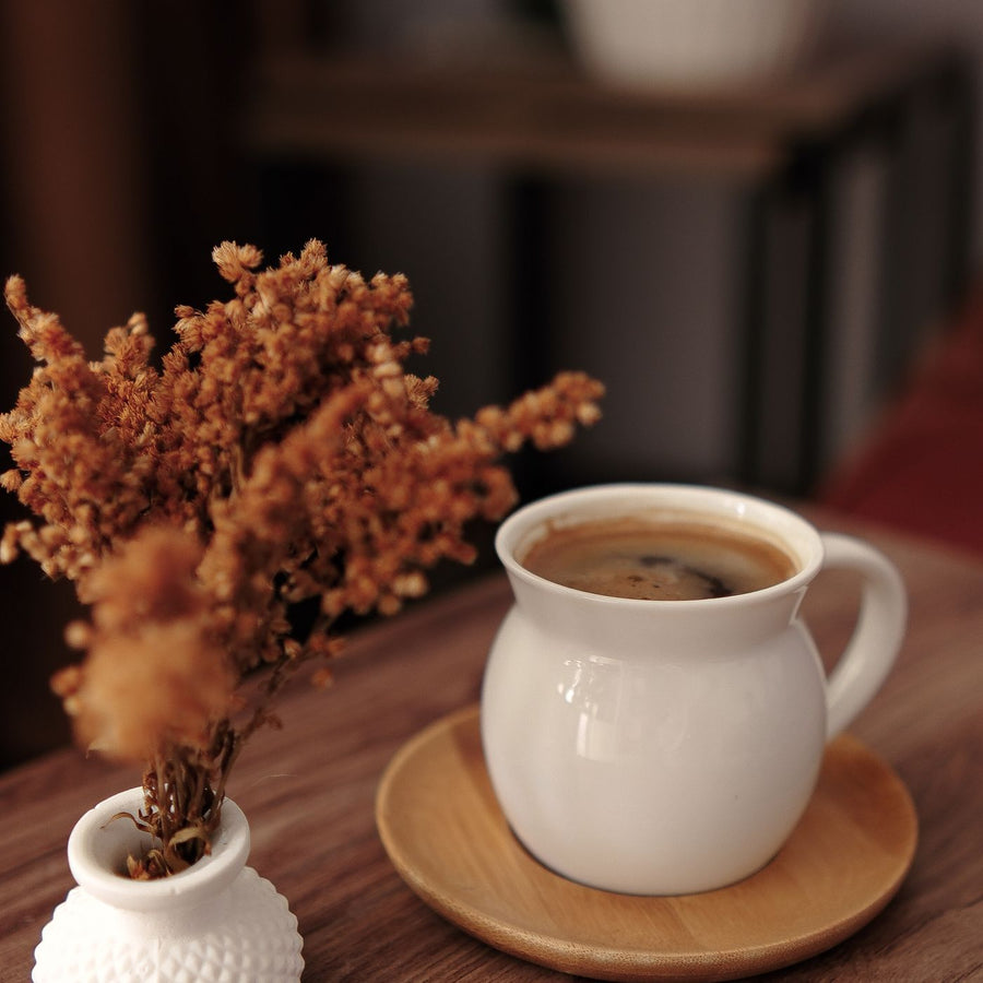 A warm toned coffee mug on a wooden table with dried flowers laid beside it.