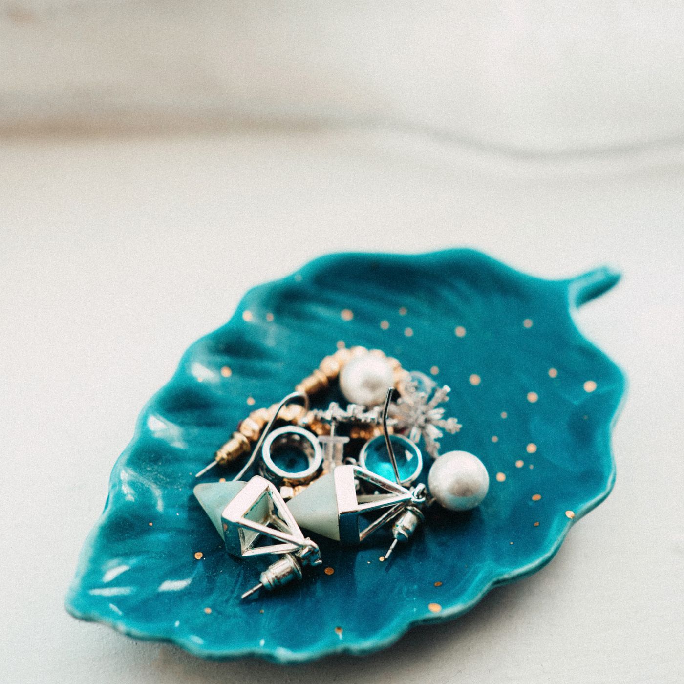 A small blue ceramic dish, photographed with assorted jewellery resting in it.
