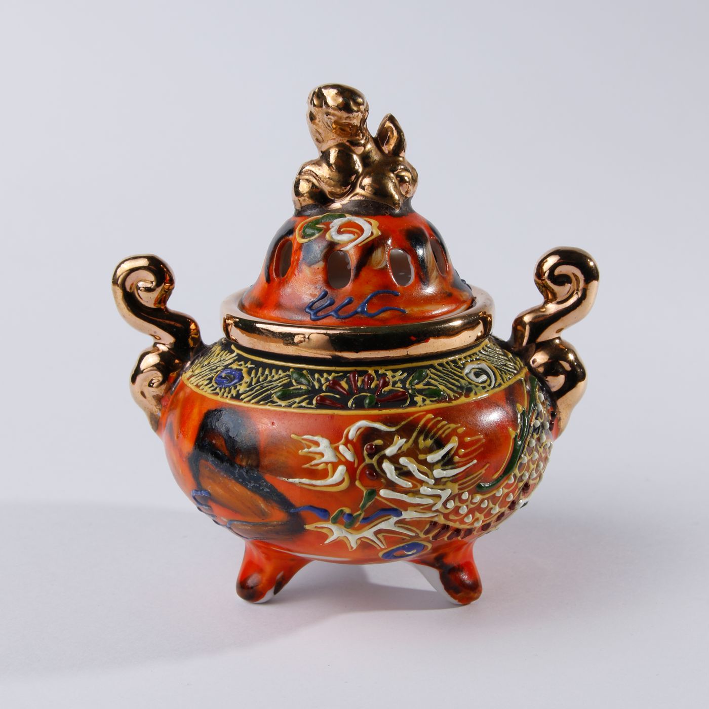 An oriental incense burner carrying a dragon motif in deep rich colours.