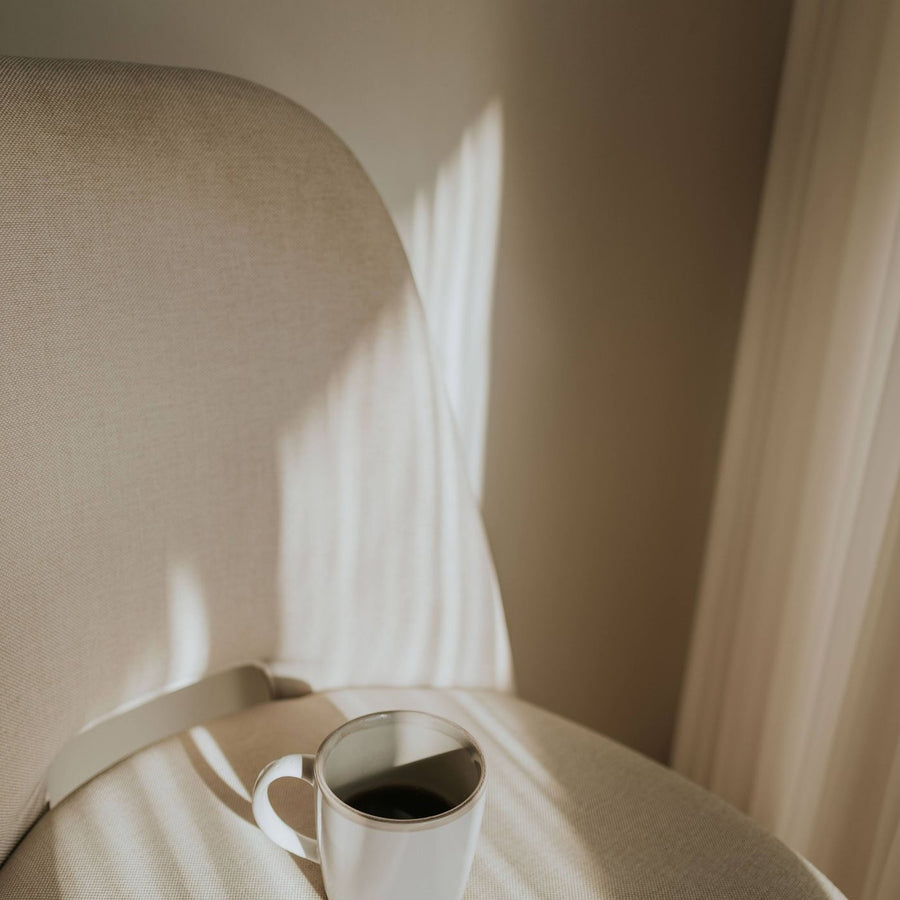 A white coffee cup left on a chair, with sunlight throwing hard shadows across the seat.