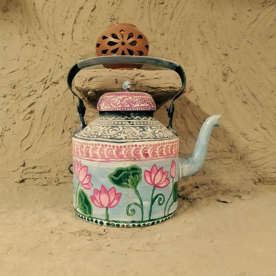 An ornate kettle worked with a lotus design, photographed against a clay wall.