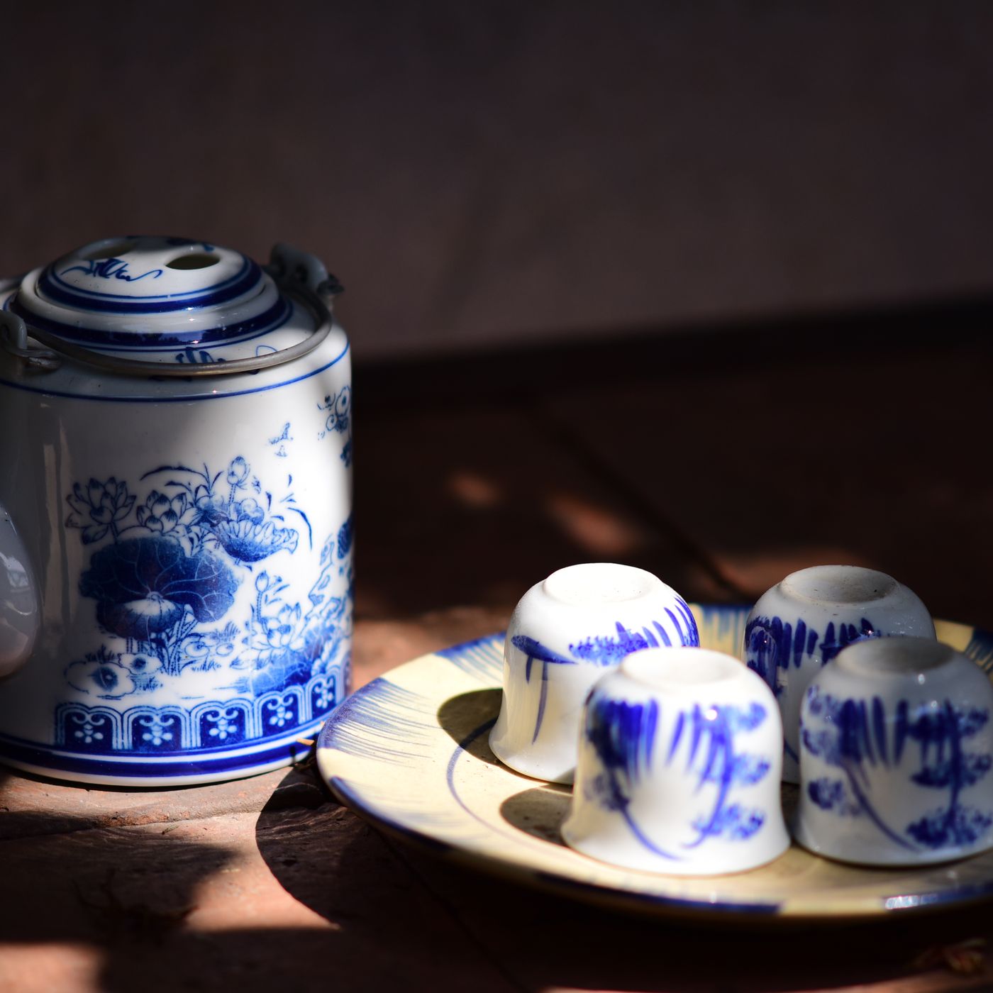 A vintage style blue and white teapot with its matching cups, shown together on a wooden table.