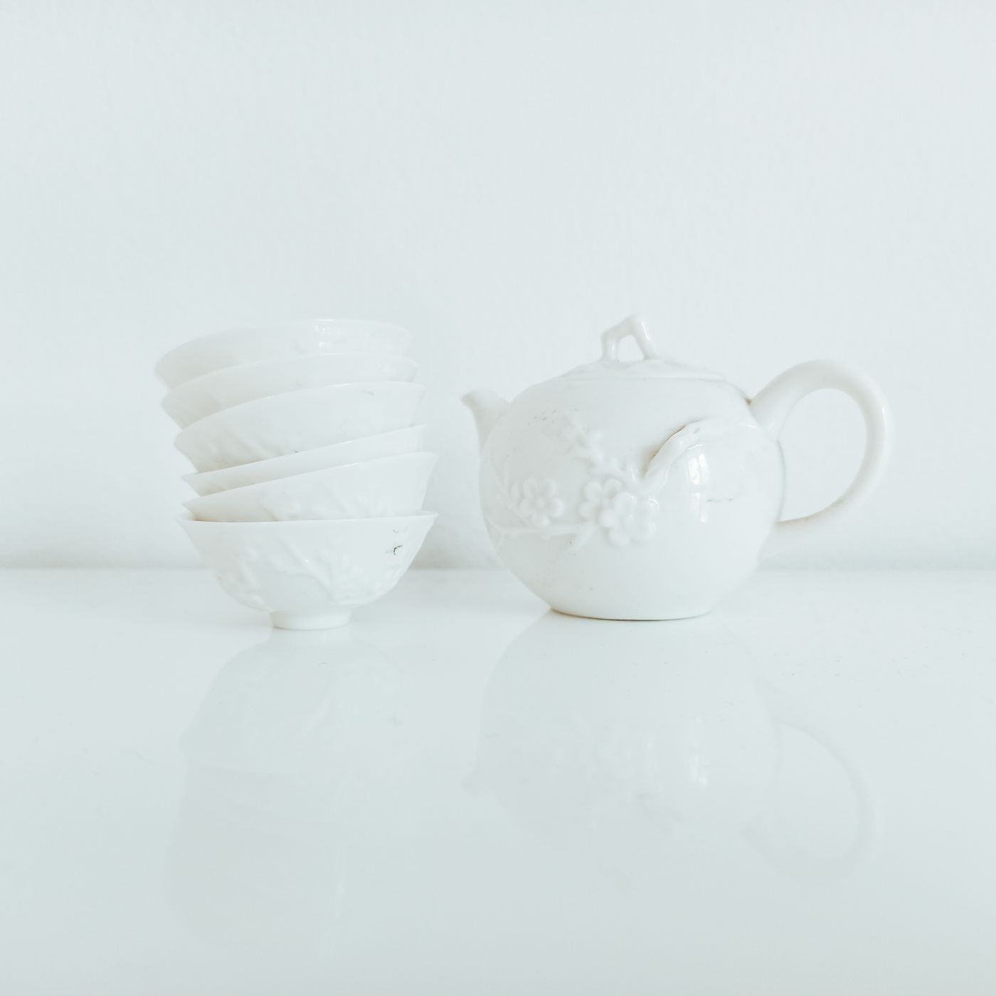 A white ceramic teapot in an old fashioned shape, set on a polished table near chawan bowls.