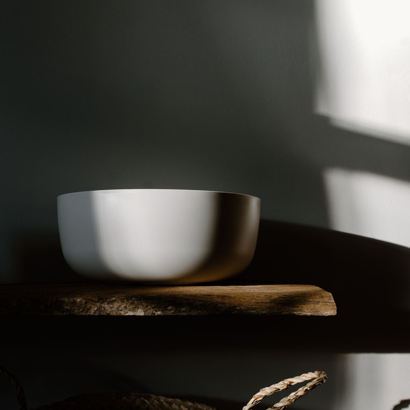 A plain white bowl on a wooden surface in soft daylight.
