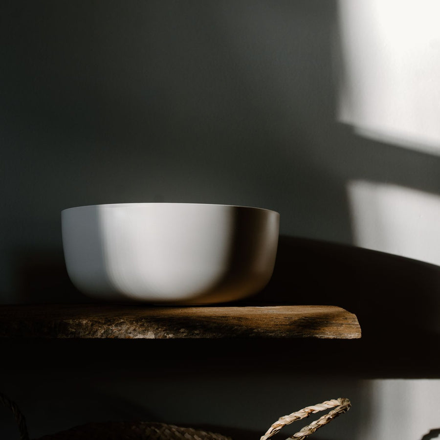 A plain white bowl on a wooden surface in soft daylight.