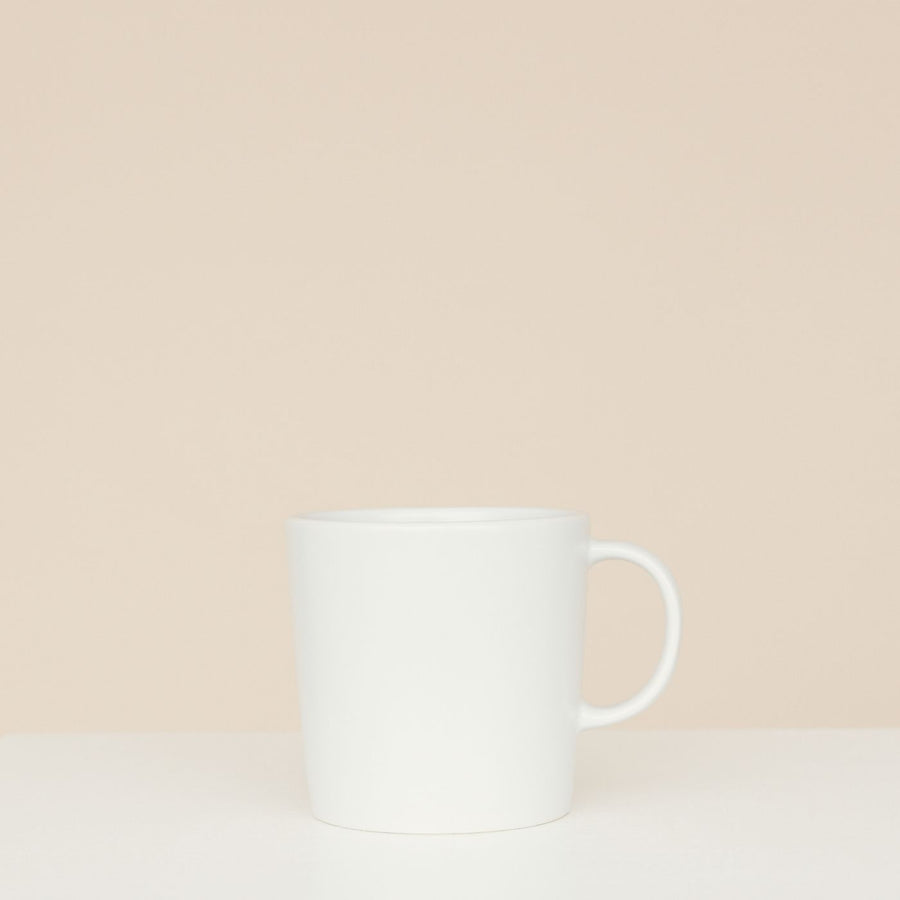 A simple white ceramic mug shown on a neutral beige background with nothing else in frame.