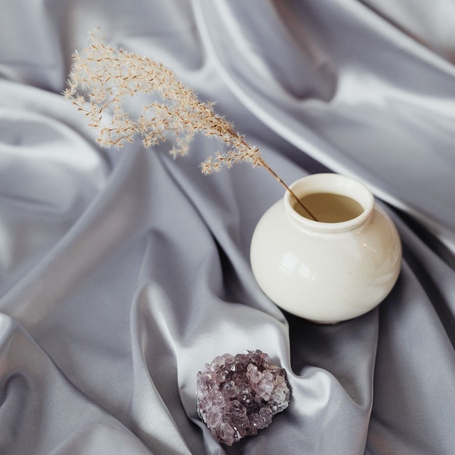 A white vase photographed as a still life with an amethyst crystal and a length of silk.