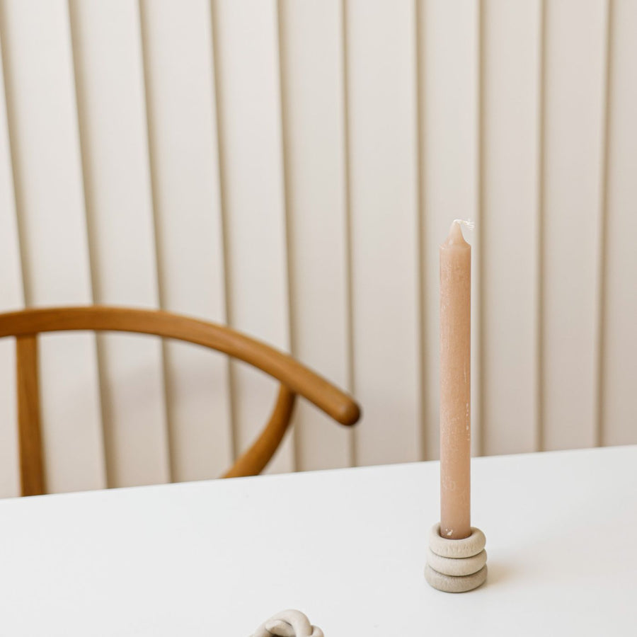 A clay candle holder on a modern white table holding a beige candle.