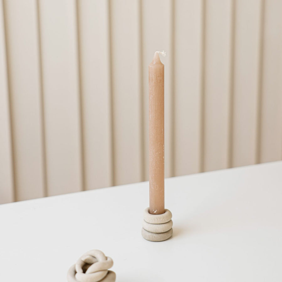 A clay candle holder in a plain minimal setting with a candle standing in it.