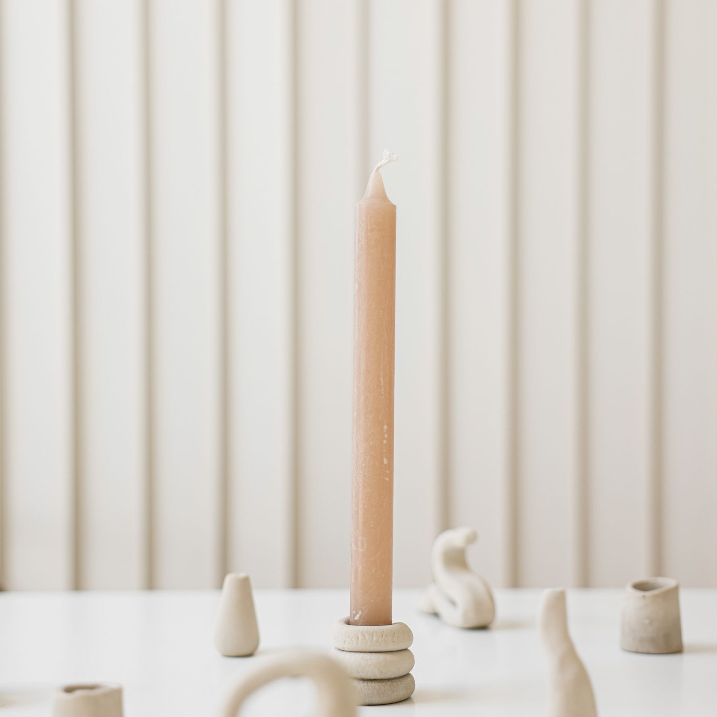 A clay candle holder photographed on a white table with a wax candle beside it.