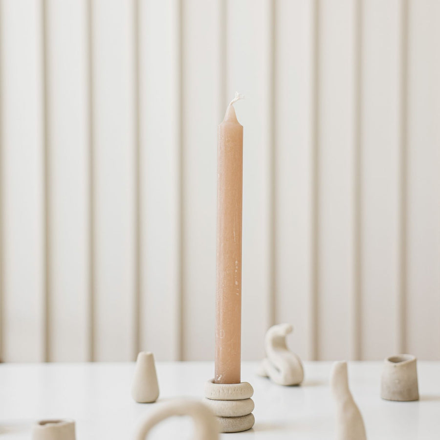 A clay candle holder photographed on a white table with a wax candle beside it.