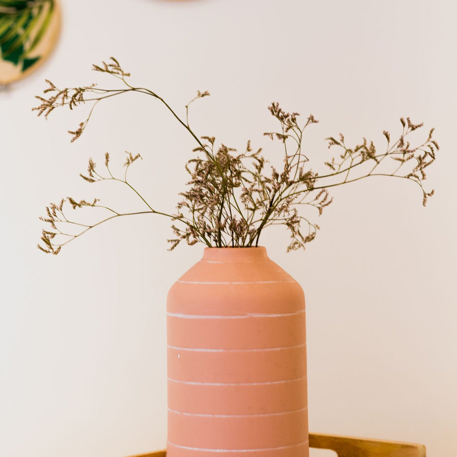 A terracotta vase standing in a wooden tray with dried flowers in it.