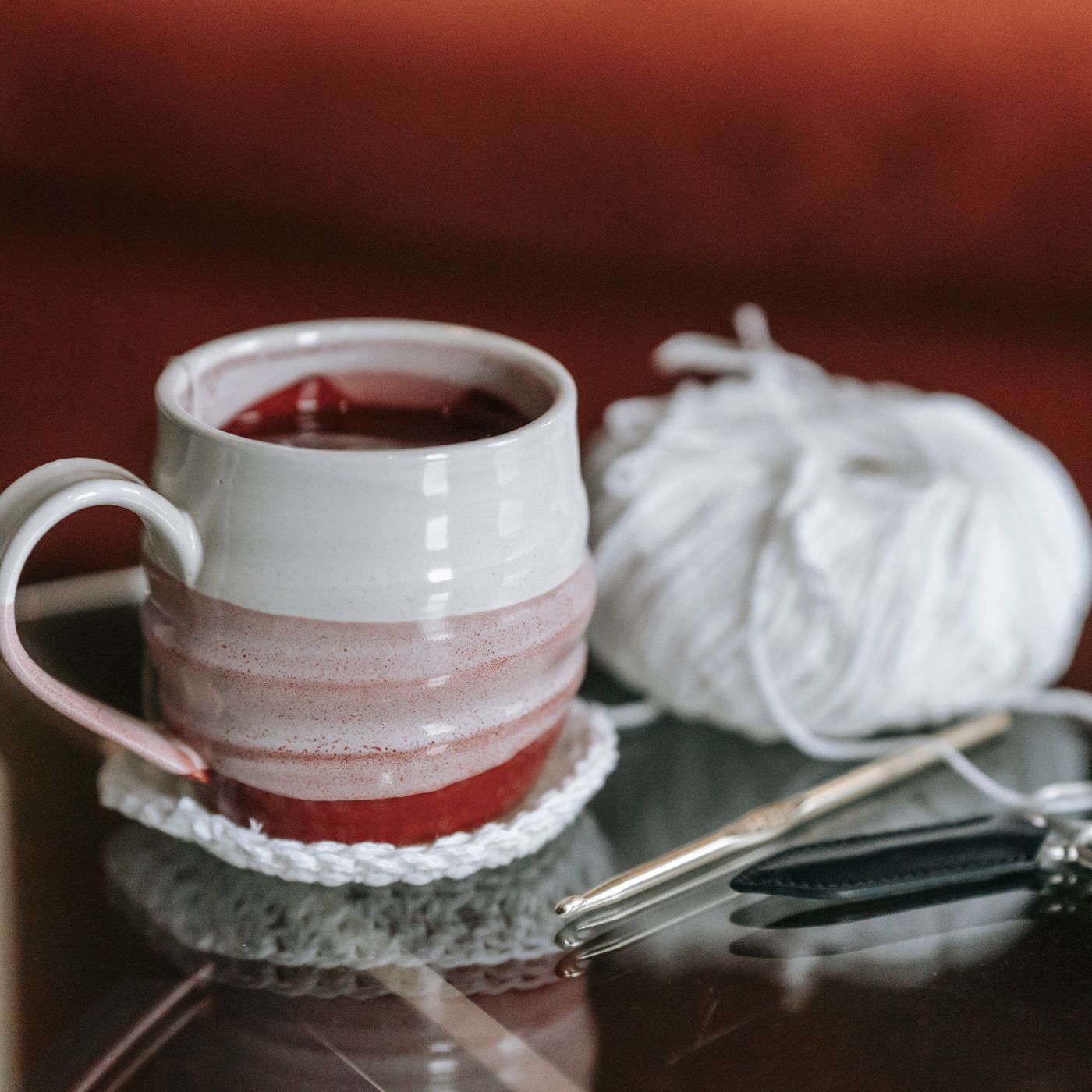A handmade mug photographed close up on a work table beside crochet and craft supplies.