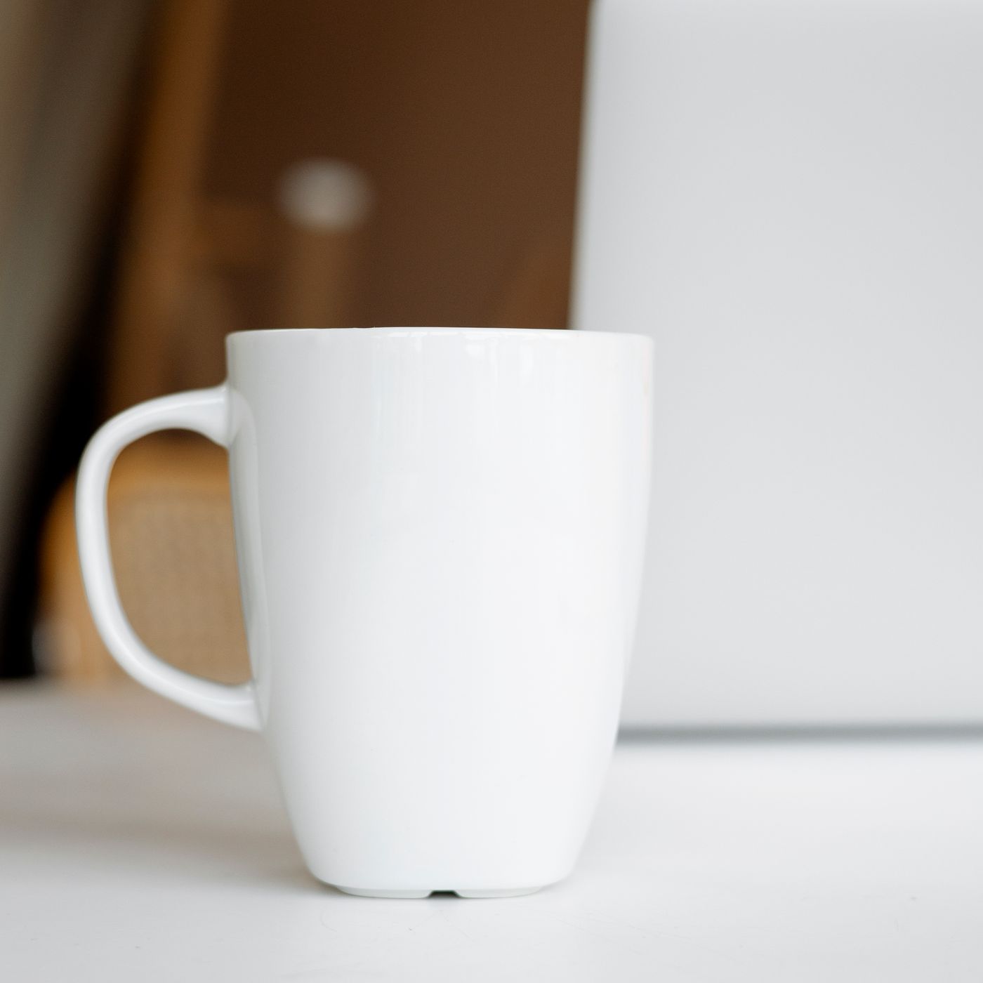 A simple white ceramic mug sitting on a desk beside a laptop.