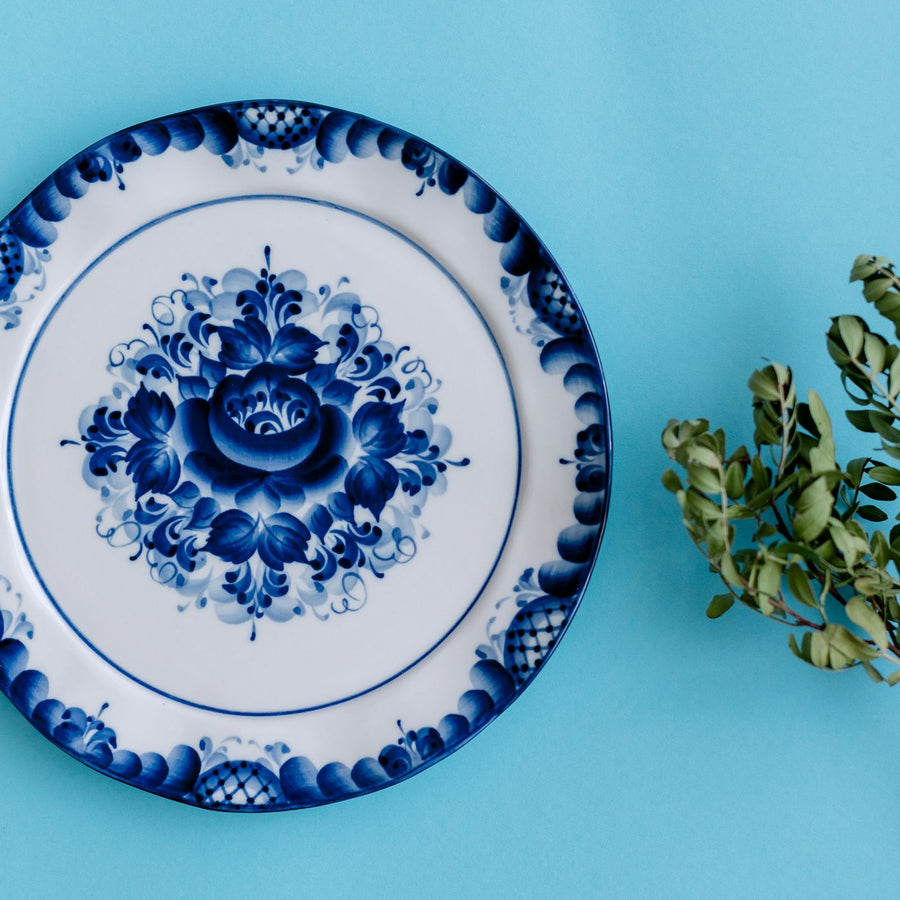 A porcelain plate worked with an intricate blue floral design, shown against a blue background.