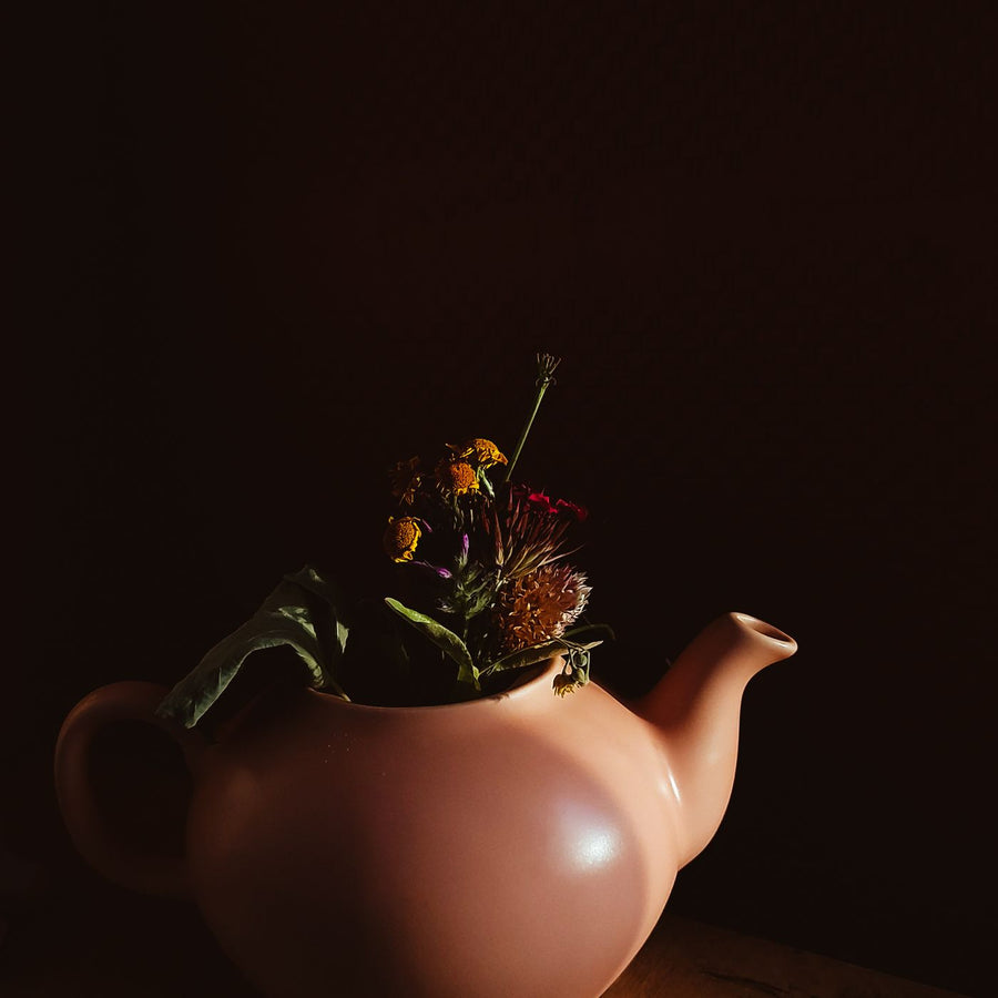 A ceramic teapot painted with bright flowers, shot against a dark backdrop.